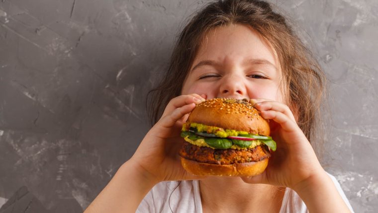 Kind beißt in veganen Hamburger